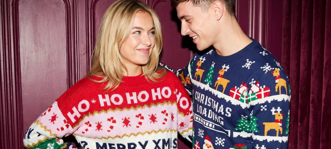 Ung kvinde og mand i farverige julesweaters smiler til hinanden foran bordeauxfarvet dør
